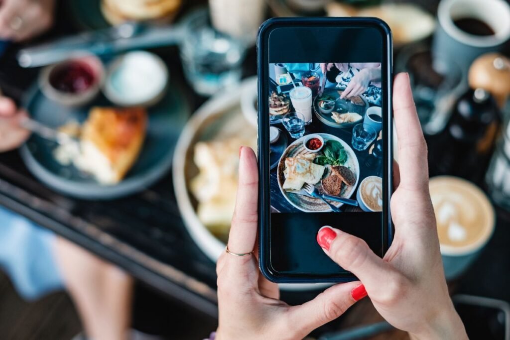 woman taking a picture on her mobile phone of a restaurant table with food